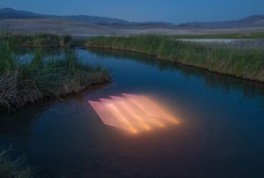 a river landscape in a desert with a peach-colored geometric light projection in the surface of the water