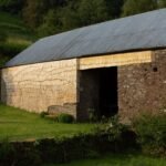 the side of an old stone barn clad in tiny wooden shingles in an undulating pattern