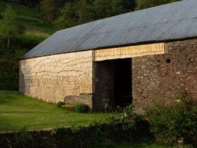 the side of an old stone barn clad in tiny wooden shingles in an undulating pattern