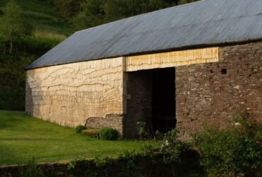 the side of an old stone barn clad in tiny wooden shingles in an undulating pattern