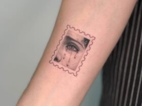 a photograph of a postage stamp-shaped tattoo on a forearm, containing a compositional detail of a woman