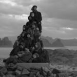 a black-and-white photograph in the Jordanian desert of a group of people in black garments perched on a stack of boxes to create a monolith-like form