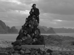 a black-and-white photograph in the Jordanian desert of a group of people in black garments perched on a stack of boxes to create a monolith-like form