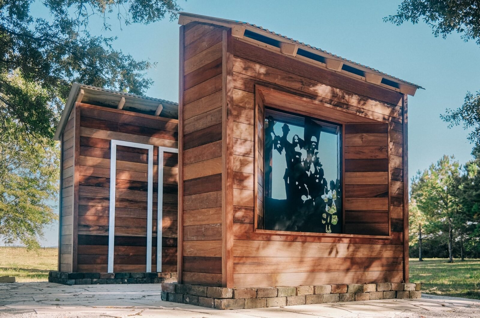 two wooden structures stand parallel. the one closest to the viewer has a metal window plate that casts a shadow of a family