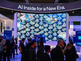 People in a blue-lit convention hall stand before a towering display with an illustration of connected communities under a sign saying "AI Inside for a New Era."