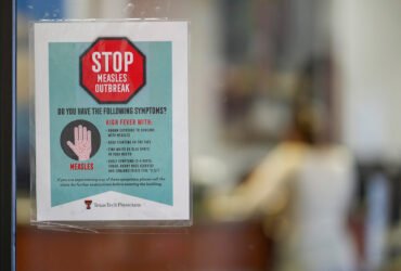 A sign taped to a door of a medical clinic in Texas reads "STOP Measles Outbreak" and lists symptoms.