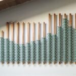 a wood and rope installation of sage green hues hangs on a wall