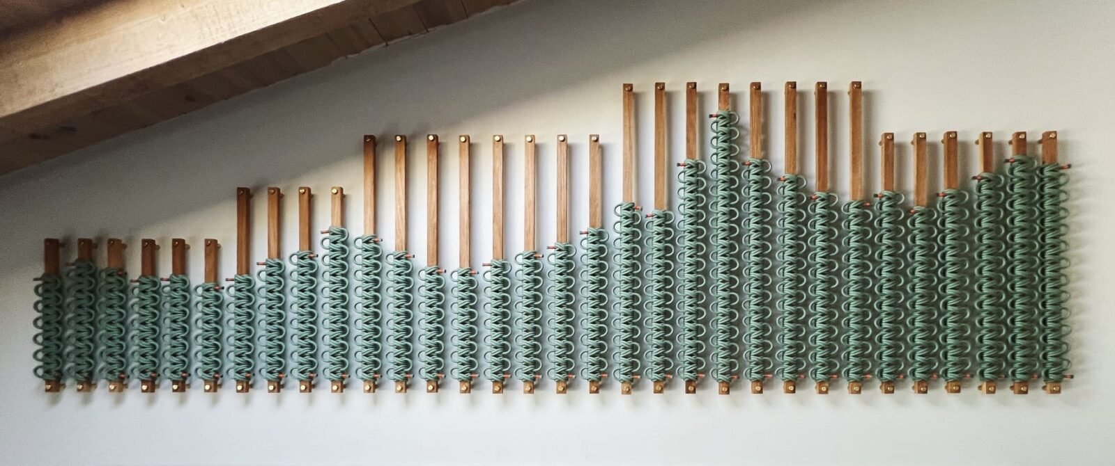 a wood and rope installation of sage green hues hangs on a wall