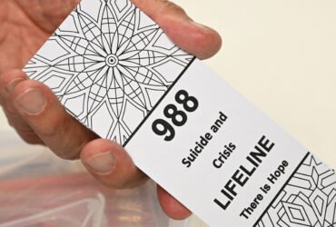 A photo of a hand holding a card that reads "988 Suicide and Crisis Lifeline There is Hope"