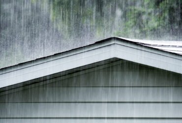 A photo shows raindrops falling on a shingle roof.