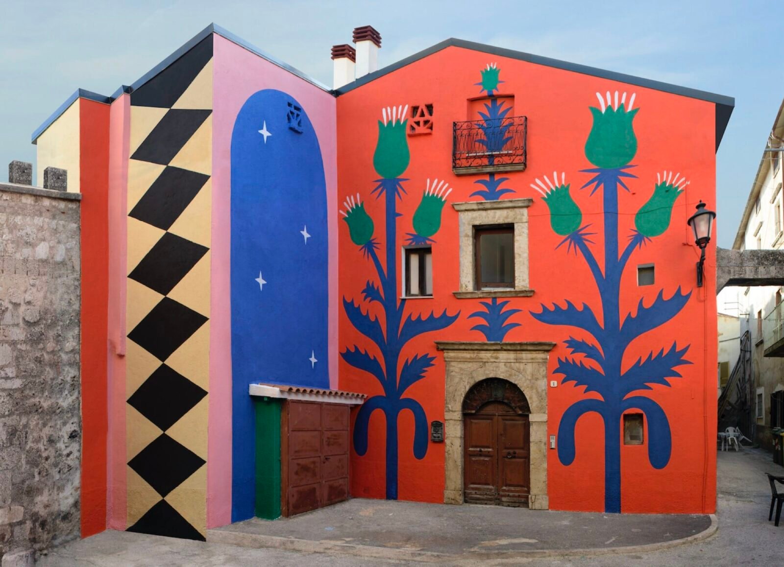 part of a mural on a two-story building in Italy, with a red background and geometric patterns and thistle designs