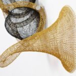 detail of a gold and black abstract woven metal sculpture with tubes and circular forms on a wall