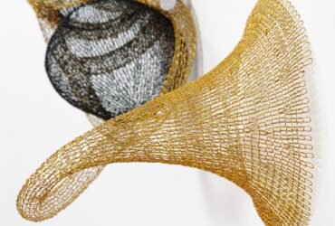 detail of a gold and black abstract woven metal sculpture with tubes and circular forms on a wall