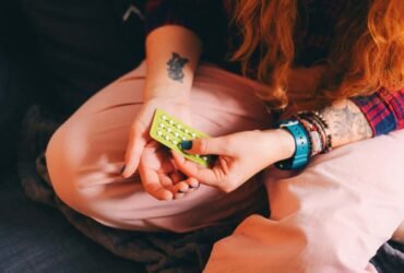 Description: A young woman sits on a comfortable couch, holding a blister pack of birth control pills. This candid shot captures a personal moment related to contraceptive use and hormone therapy, emphasizing the importance of reproductive health. Perfect for themes around women???s health, contraception, hormone therapy, and self-care, this image can be used to highlight modern health choices in a relaxed, home environment.