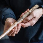 A pair of hands holding a spearlike tool made of whale bone, about a foot long