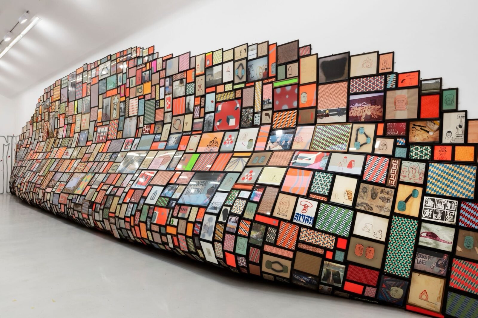 a large-scale installation along a white gallery wall, which looks like a giant slumped surface that is completely covered in a grid of tiny images