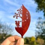 a cut leaf artwork of a squirrel under a tree