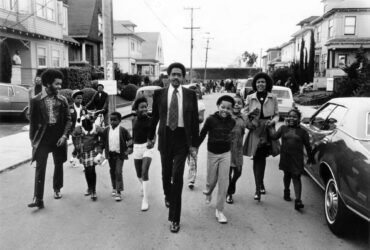 a black-and-white photo of Black Panther founder Bobby Seale and others walking down a street