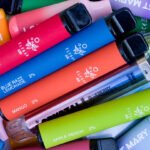 A pile of colorful disposable vape pens with various flavors labeled, such as strawberry ice, blue razz lemonade, mango, apple peach and blueberry raspberry.
