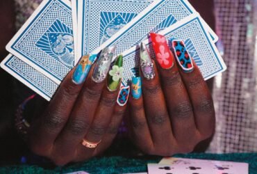 a pair of hands holding playing cards, showing off nails with intricate patterns and bright designs