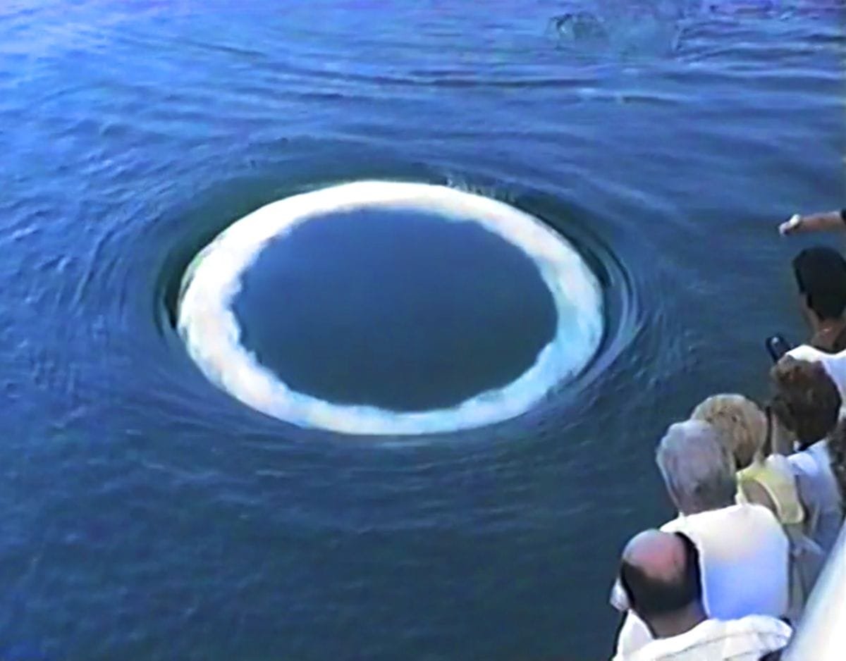 a group of people watch a white ring appear in the ocean