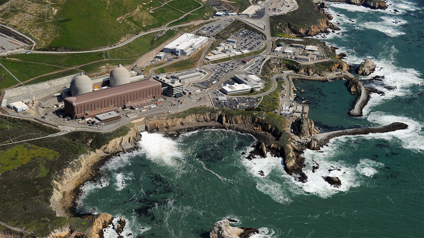 Aerial shot of the Diablo Canyon power plant, California’s last operational nuclear energy source. We see a craggy coast line surrounding the plant and areas of frothy white ocean near the plant