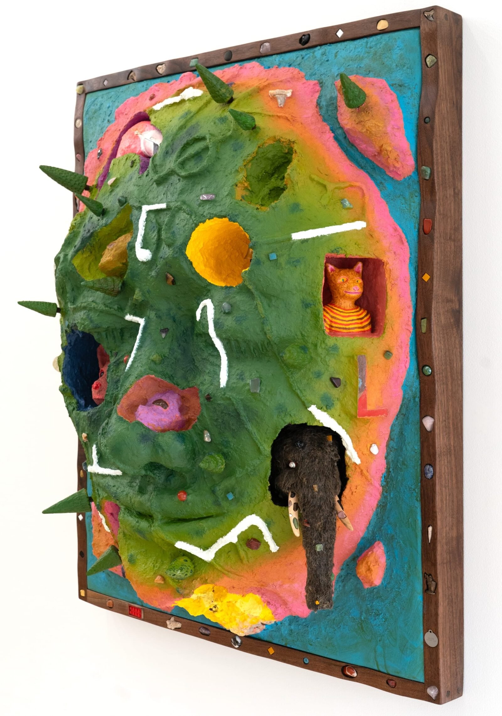 a side view of a wooly mammoth, pink animal, bell, and other objects embedded into a sculptural painting shaped like a face