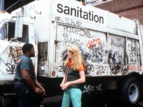 a white woman stands in front of a graffitied sanitation truck talking to a black man