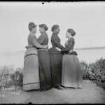 a black-and-white photo from the late 19th century of four women, turned to each other in twos and embracing
