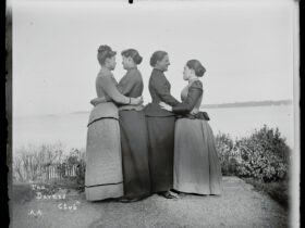 a black-and-white photo from the late 19th century of four women, turned to each other in twos and embracing