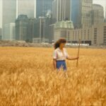 a woman in a field of wheat in front of a cityscape