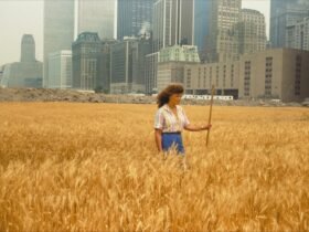a woman in a field of wheat in front of a cityscape